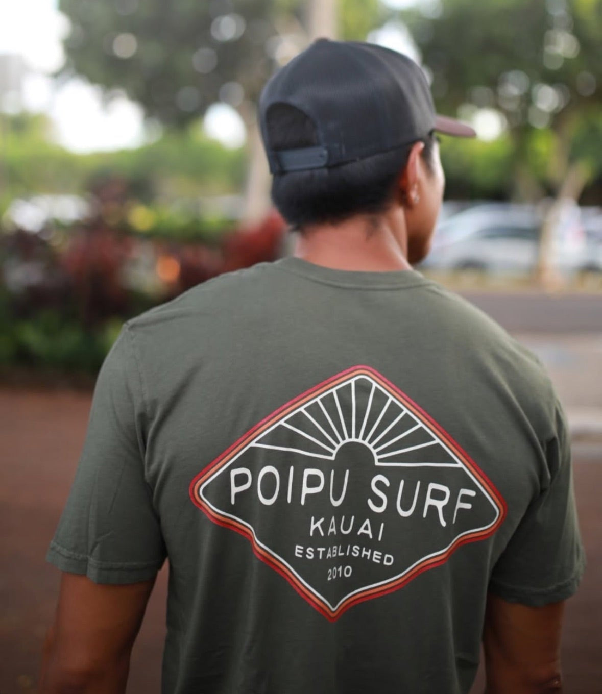Person wearing a green 'Poipu Surf' t-shirt with a blurred background